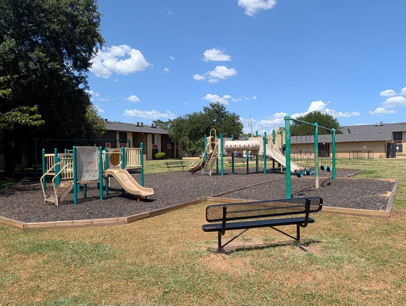 Community playground with slides, swings and benches under shade trees